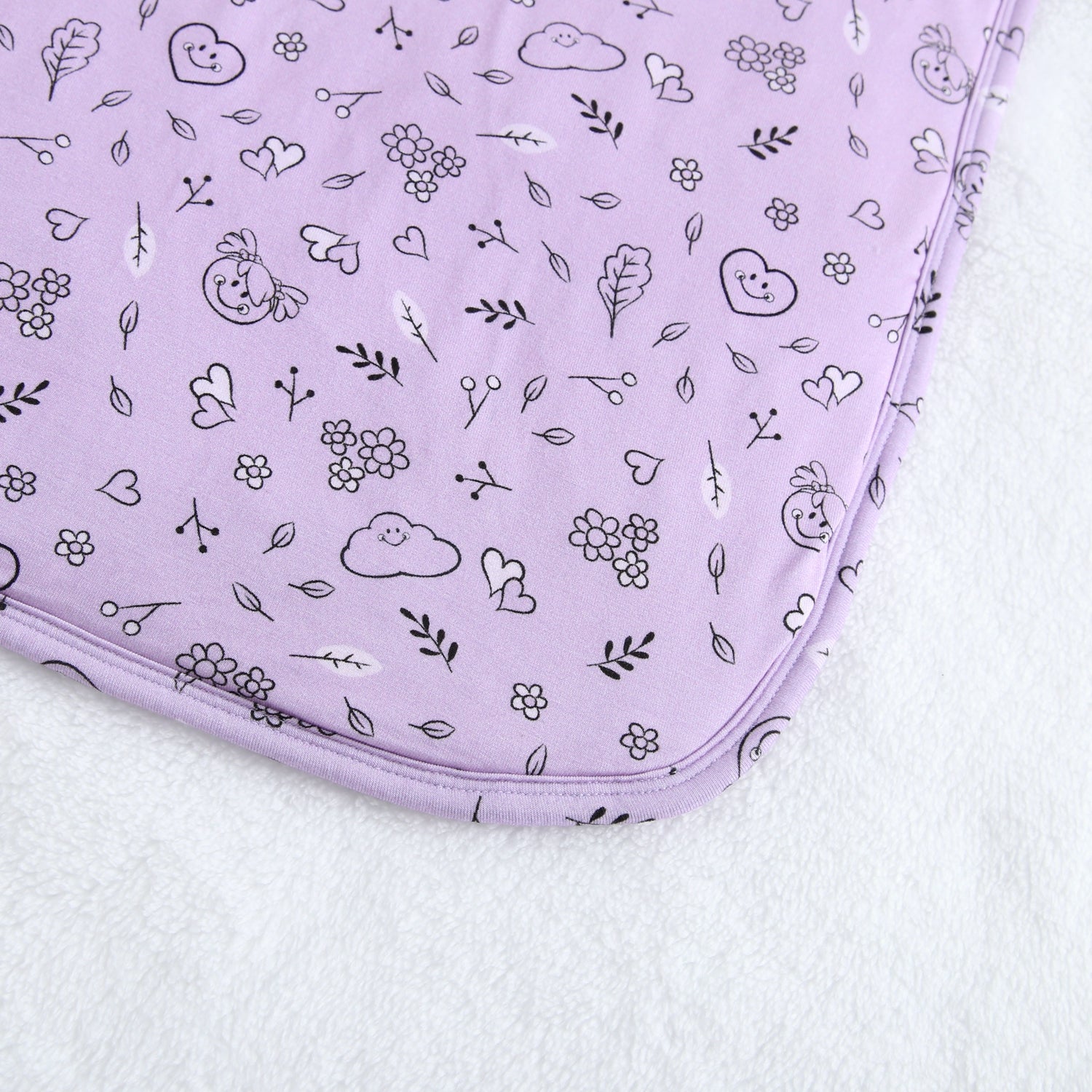 A lilac blanket with a doodle print of hearts, flowers, and clouds.