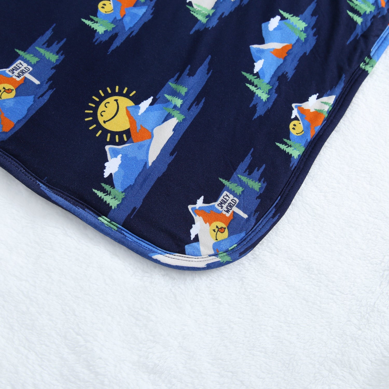 A navy blue blanket with a repeating pattern of mountains, trees, and smiling suns.