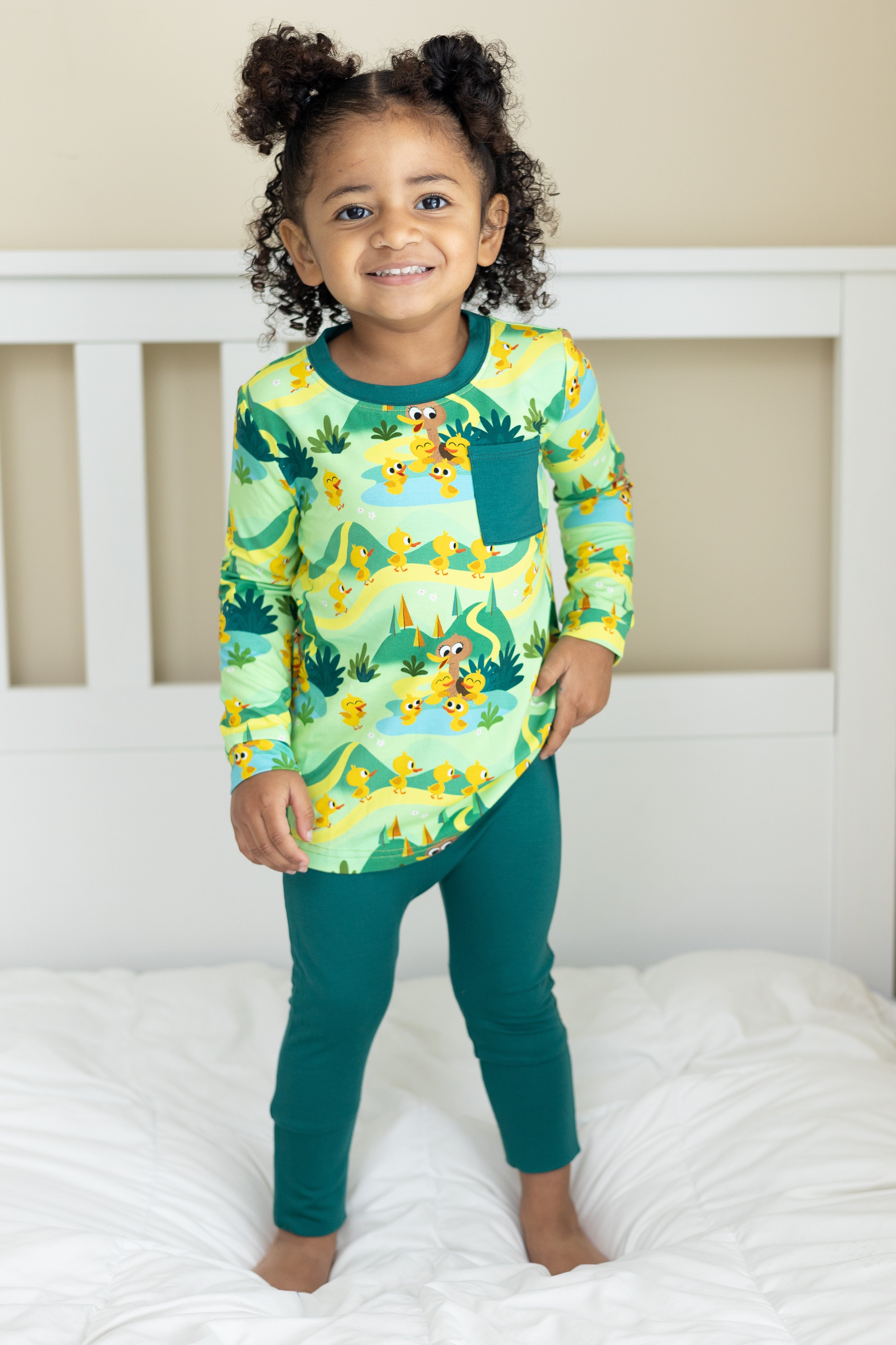 A young girl wears green bamboo pajamas with a duck pond print.