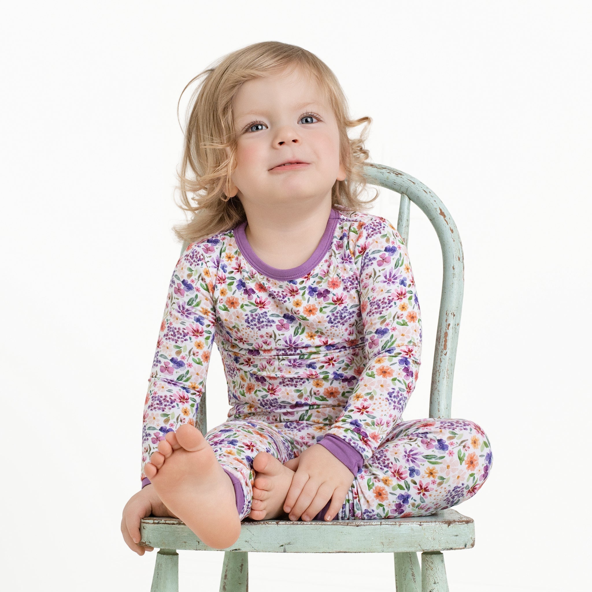 A toddler girl in floral pajamas sits on a vintage chair.