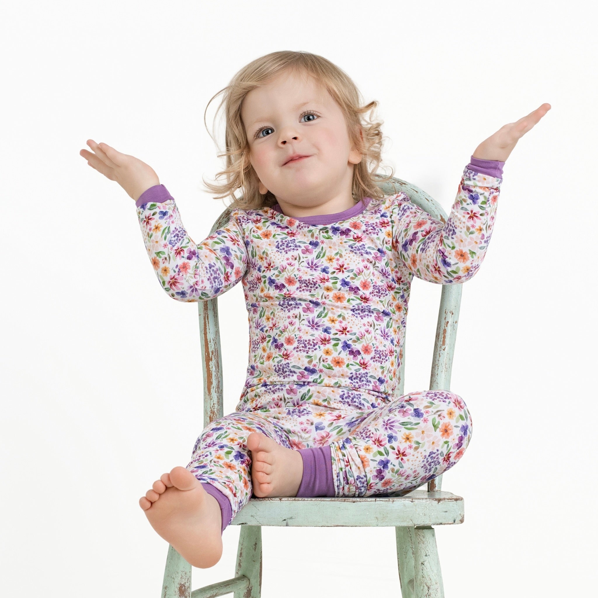 A young child sits on a chair wearing a floral print pajama set.
