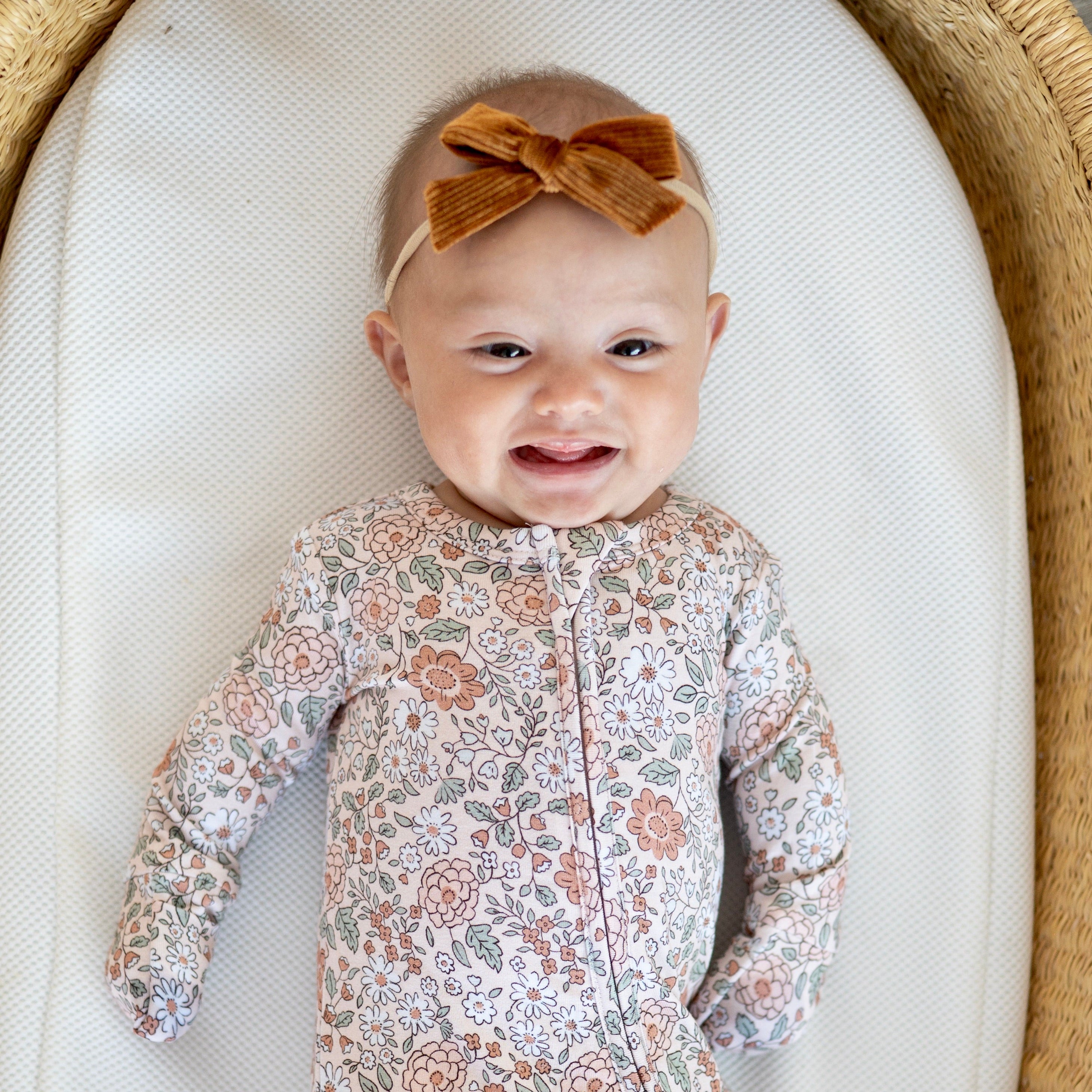 Baby in a floral outfit with a bow lying on a white surface