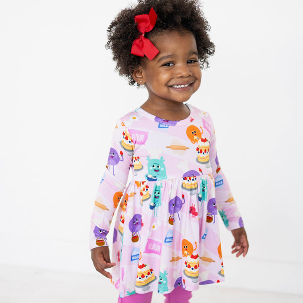 A young girl smiles wearing a pink long-sleeve peplum top with a baking-themed print.