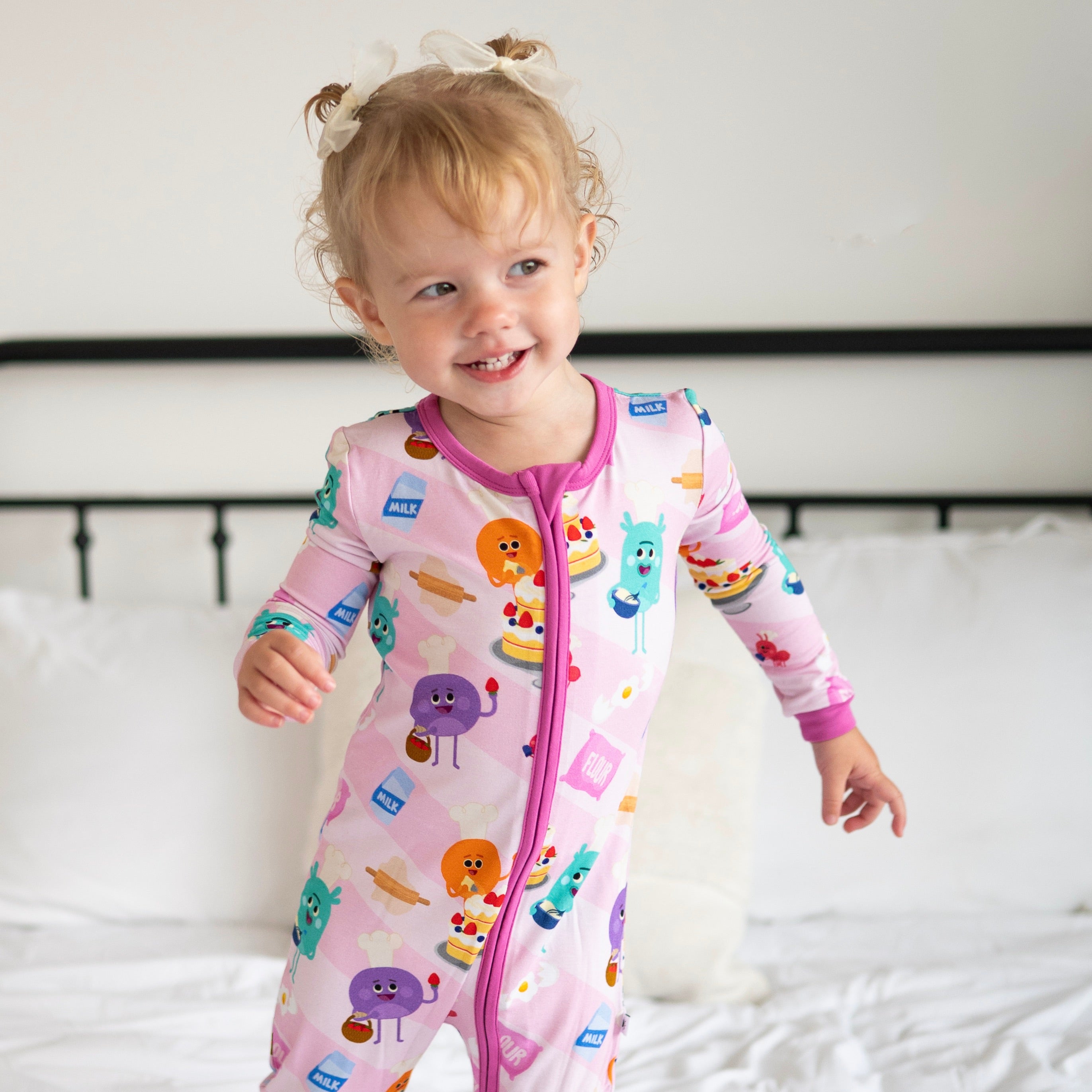 A toddler girl wears a pink bamboo pajama set with a baking-themed print.