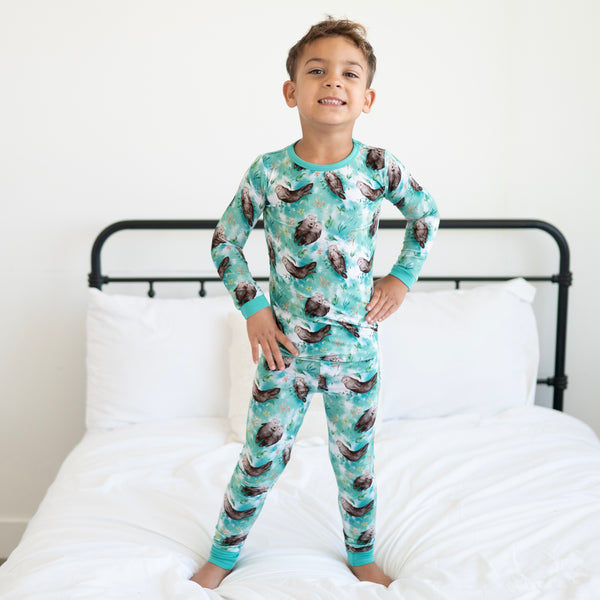 A young boy stands on a bed wearing teal pajamas with an otter print.