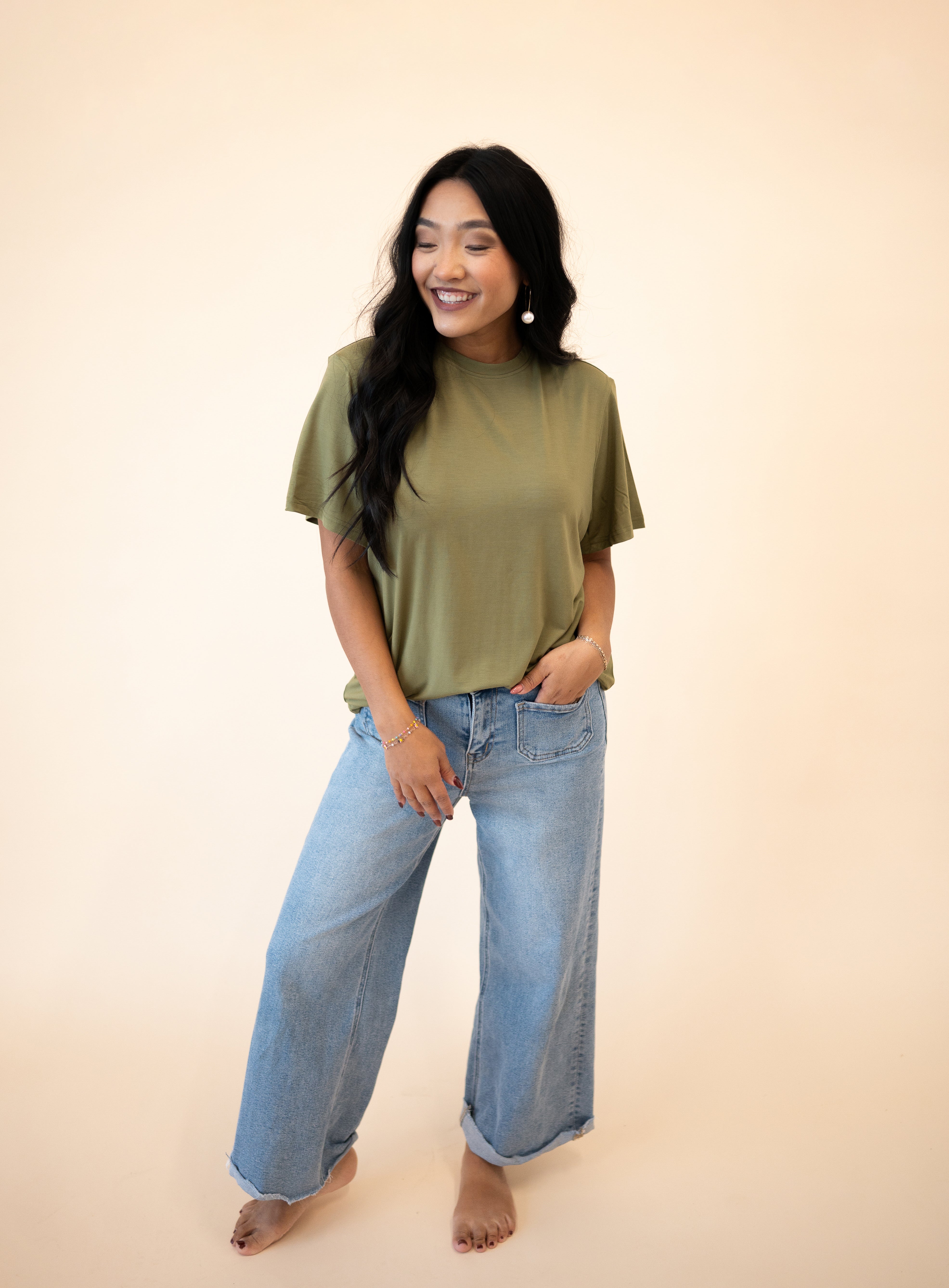 A woman wears an olive green oversized tencel modal t-shirt and light wash wide-leg jeans.