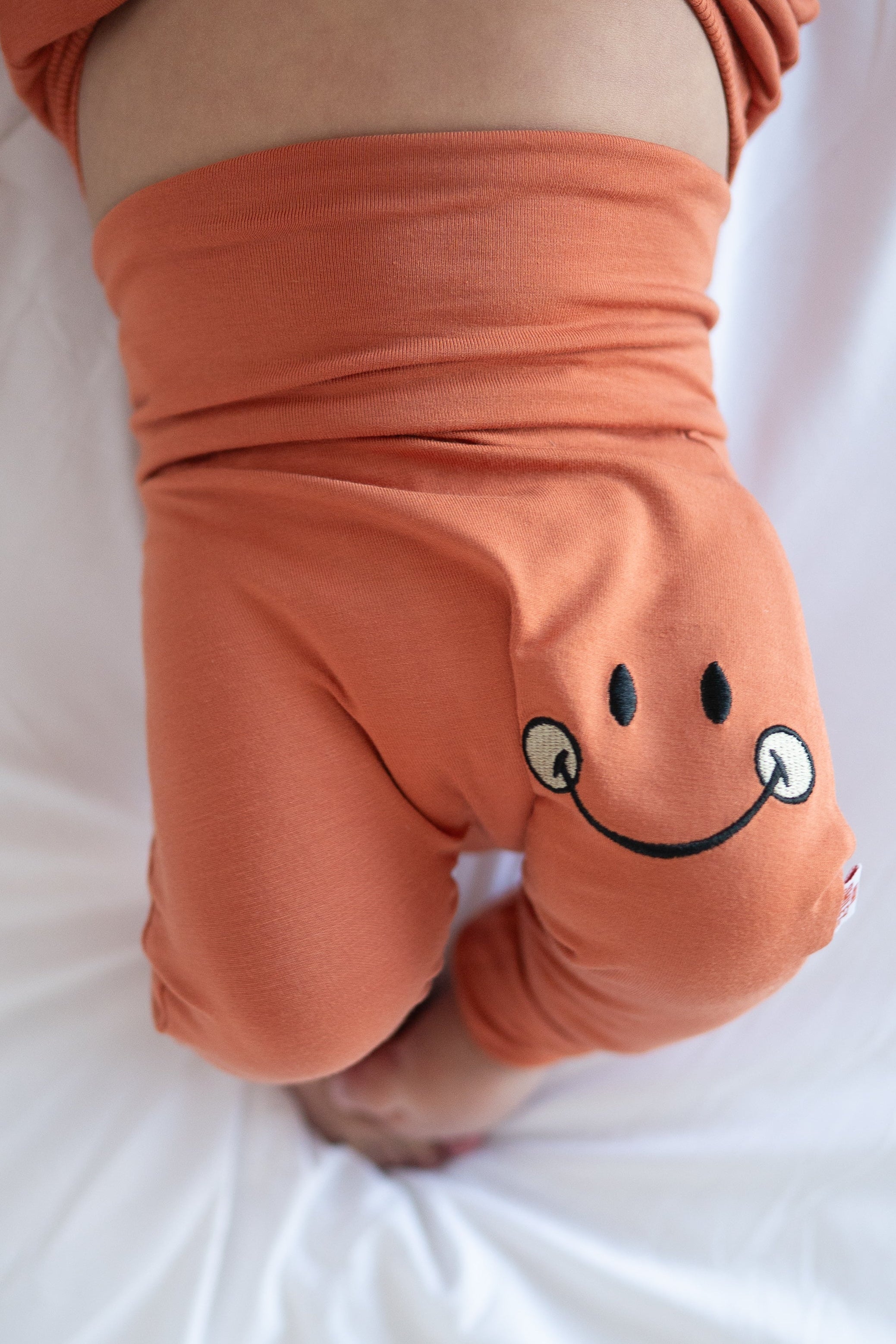 Orange bamboo baby pants with a small embroidered smiley face.