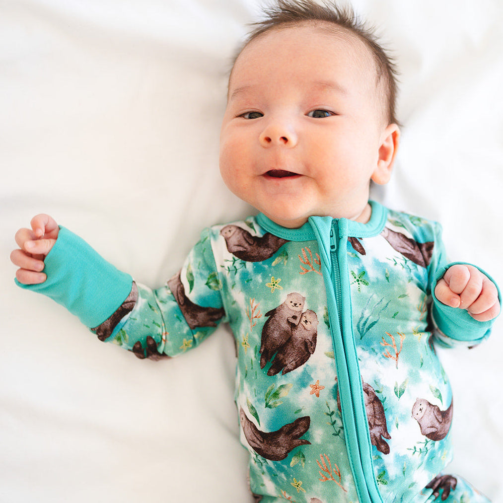 Baby wearing a teal onesie with animal prints on a white background