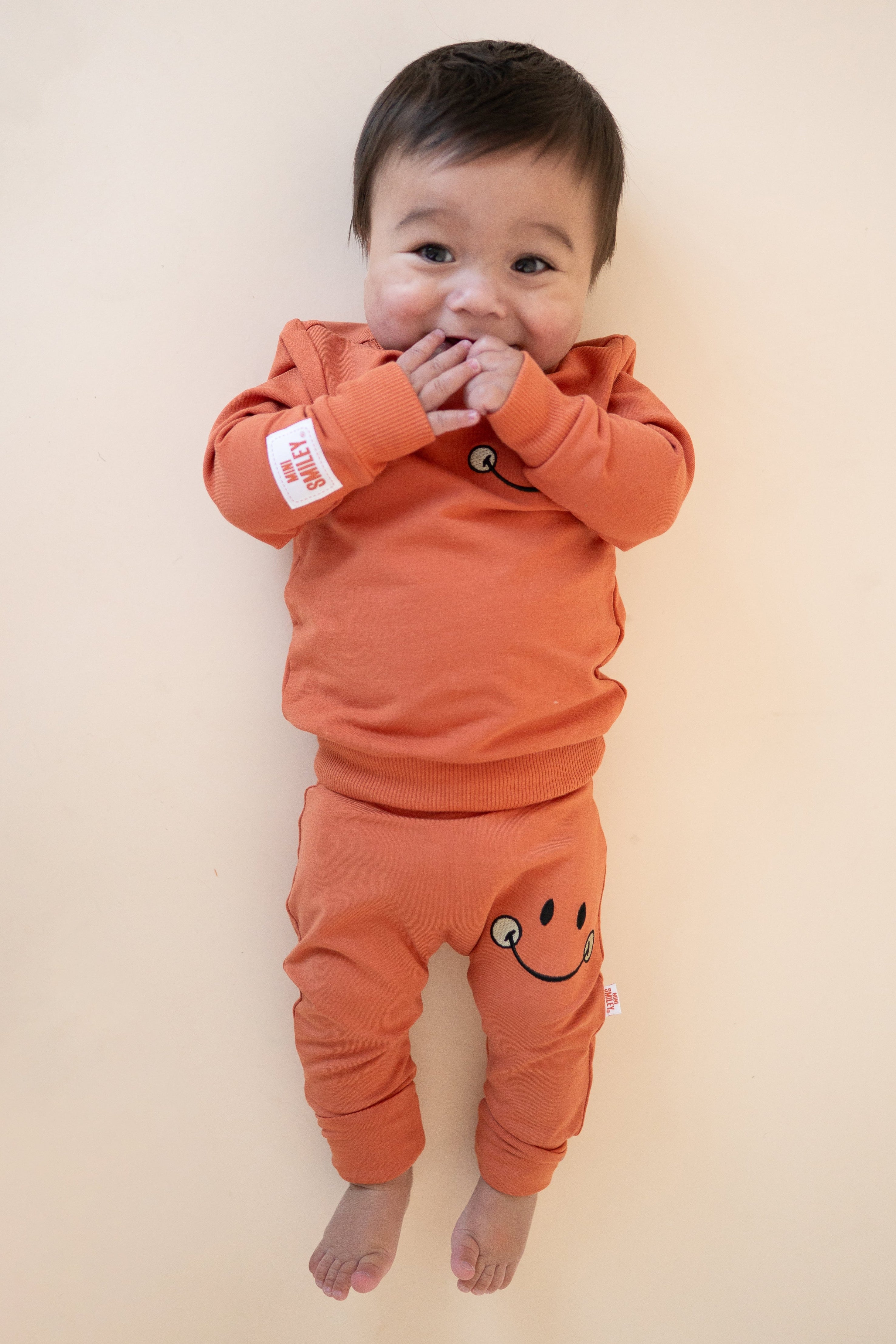 Baby in orange pants with a smiley face and matching sweatshirt.