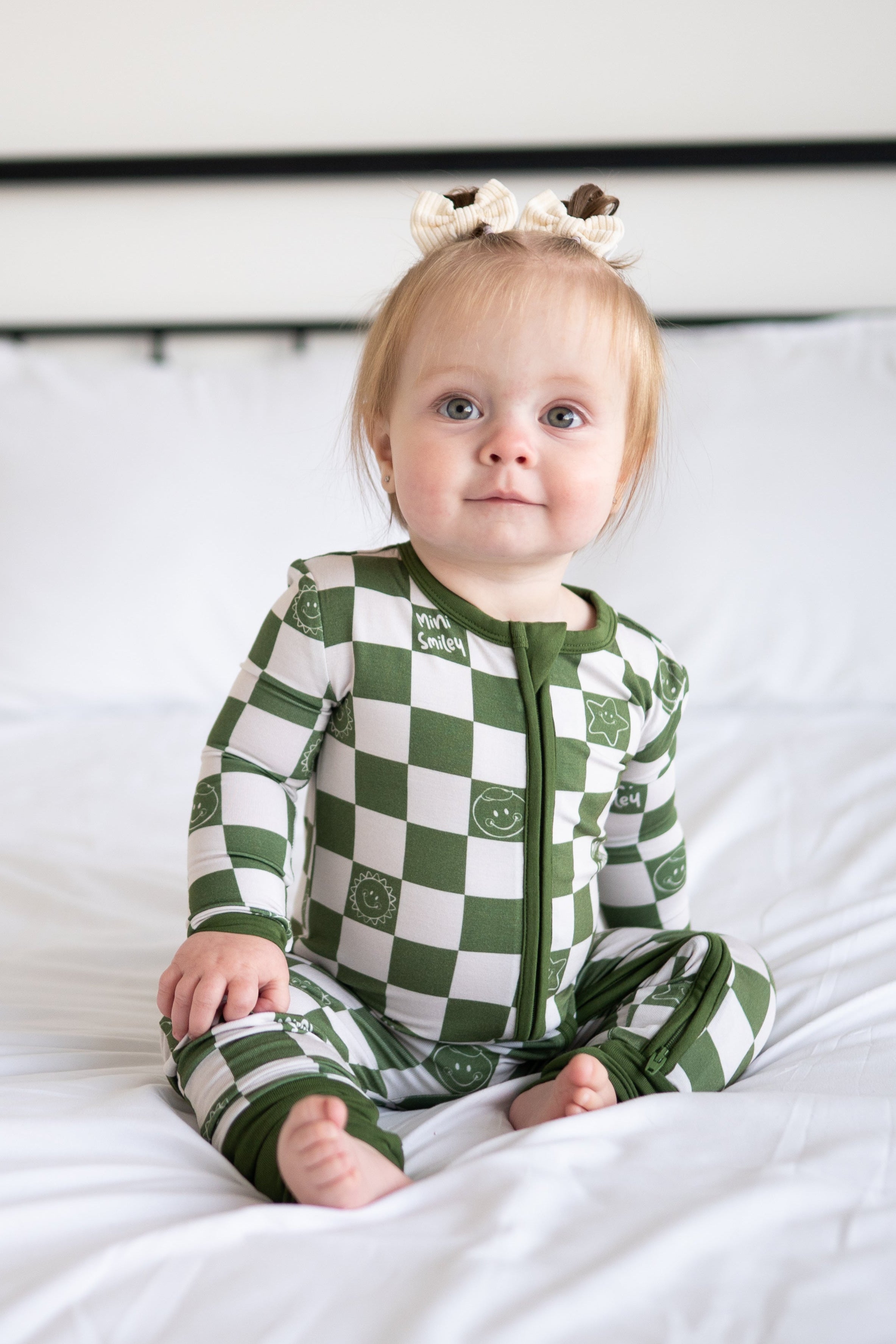 A baby girl wearing a green and white checkered bamboo pajama set with smiley faces.