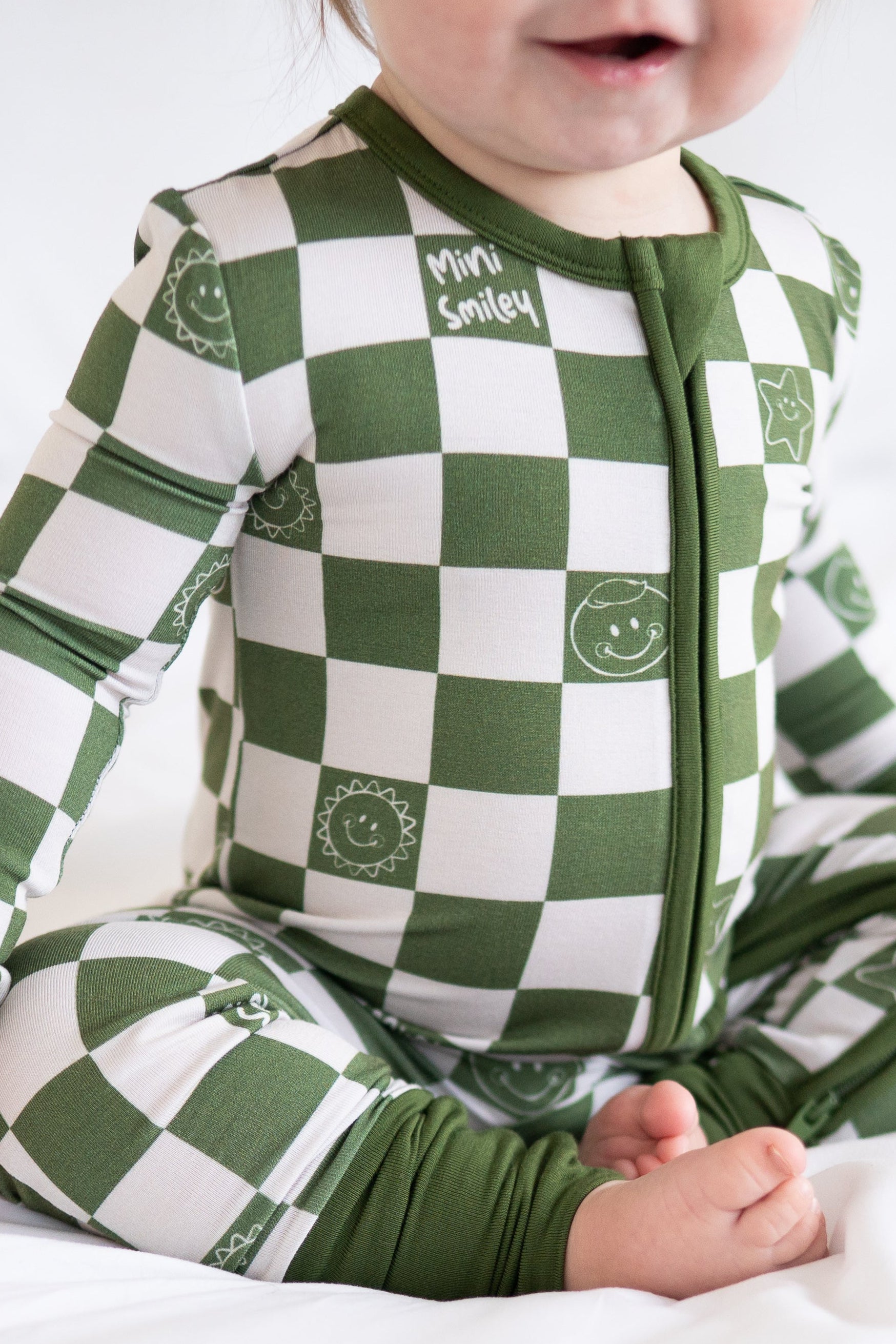 A baby wears a green and white checkered bamboo pajama set with smiley face prints.