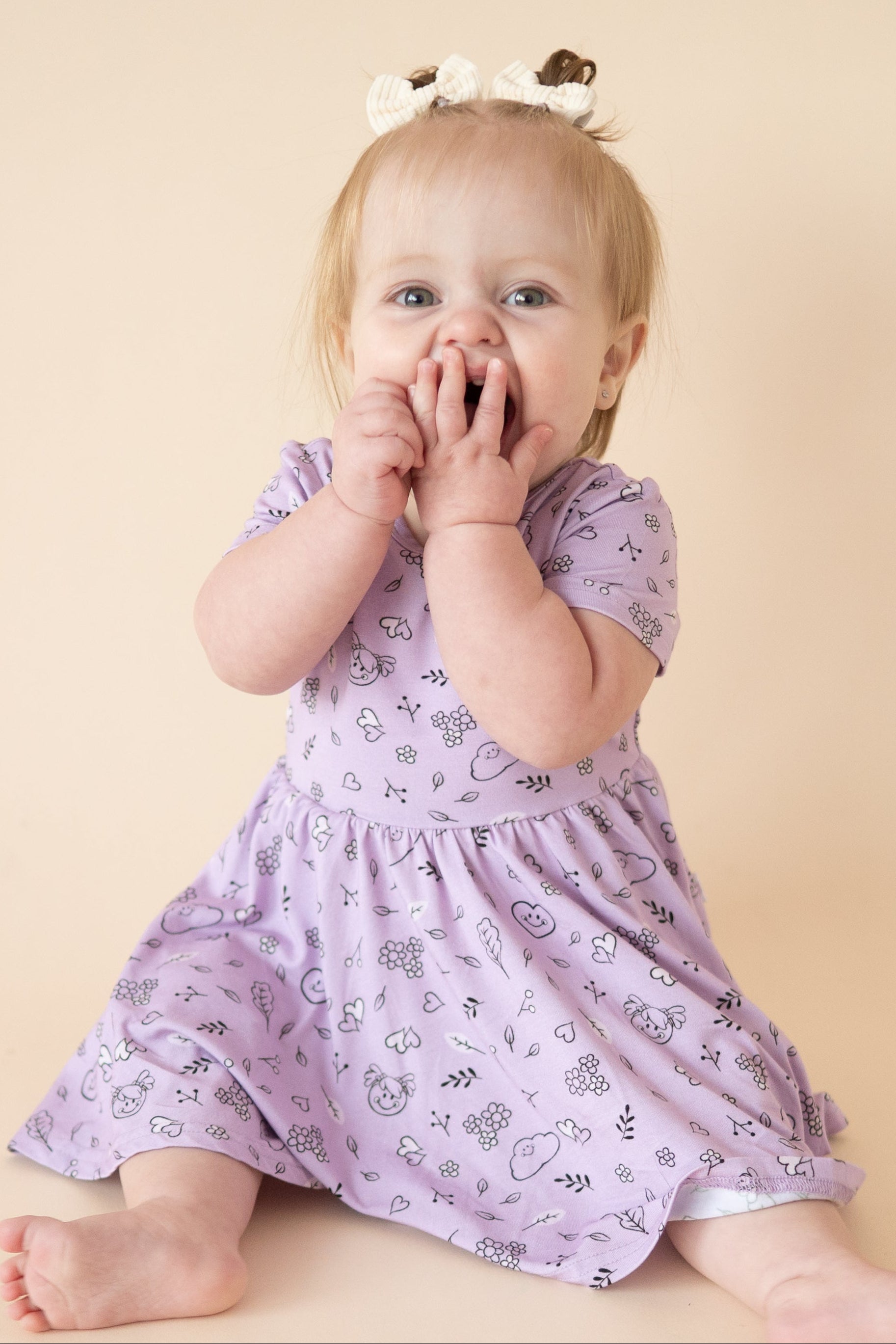 Baby in a lilac dress with a doodle print.