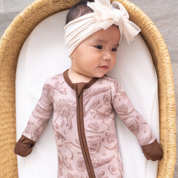 Baby in a pink bamboo pajama set with a fossil print and a white bow headband.