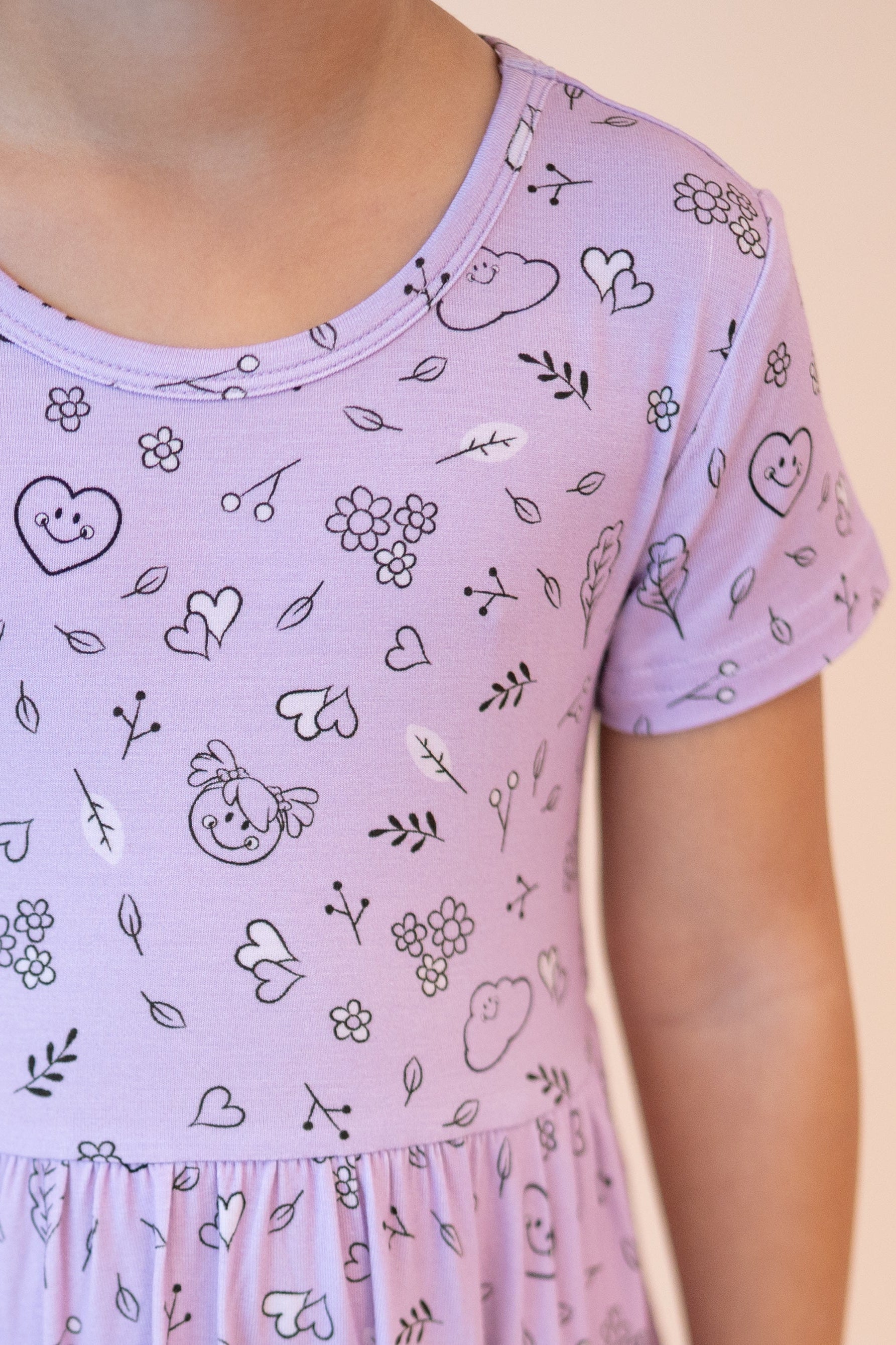A lilac dress with a doodle print of smiley faces, hearts, and flowers.