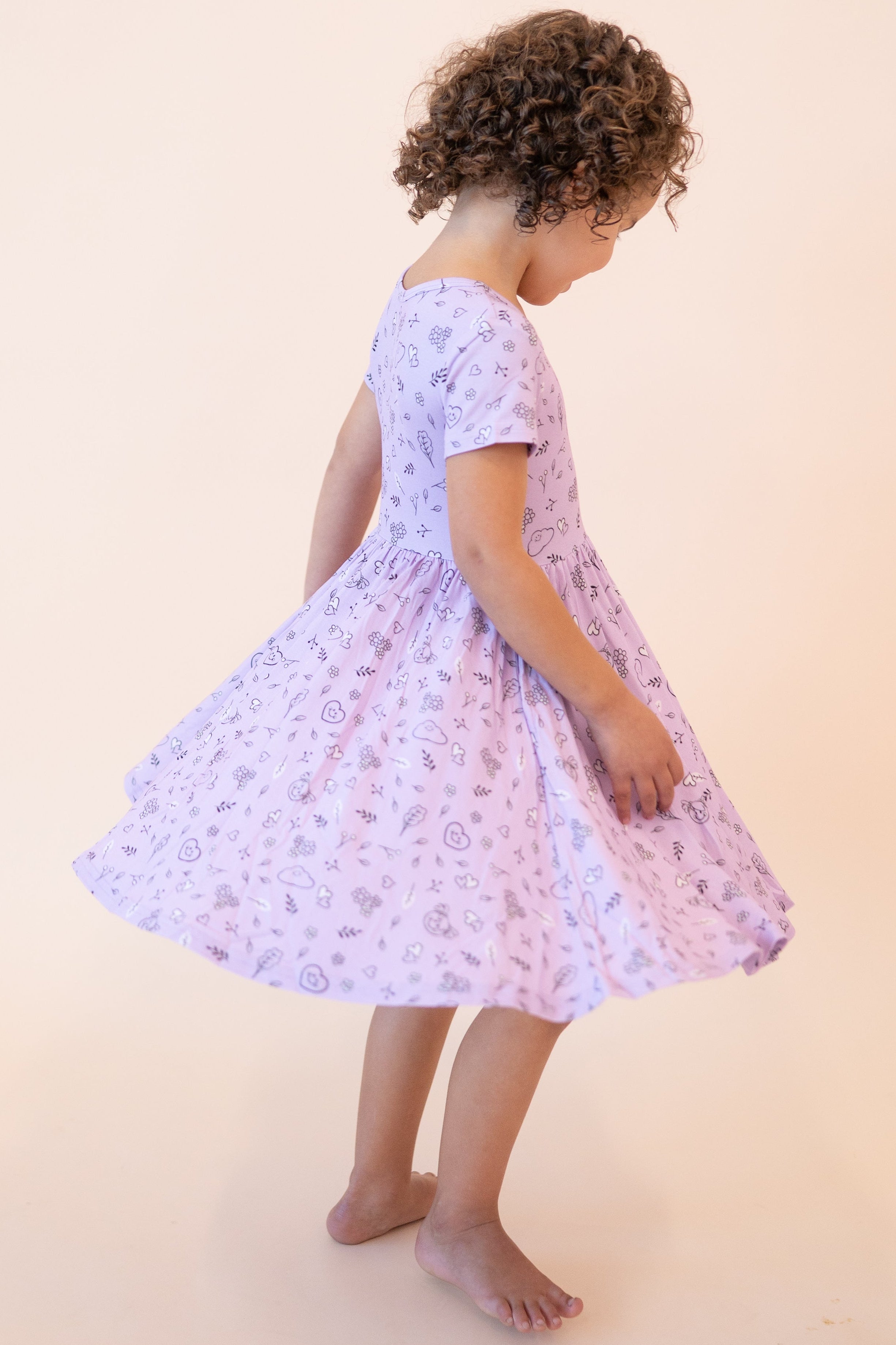 A young girl twirls in a lilac dress with a doodle print.