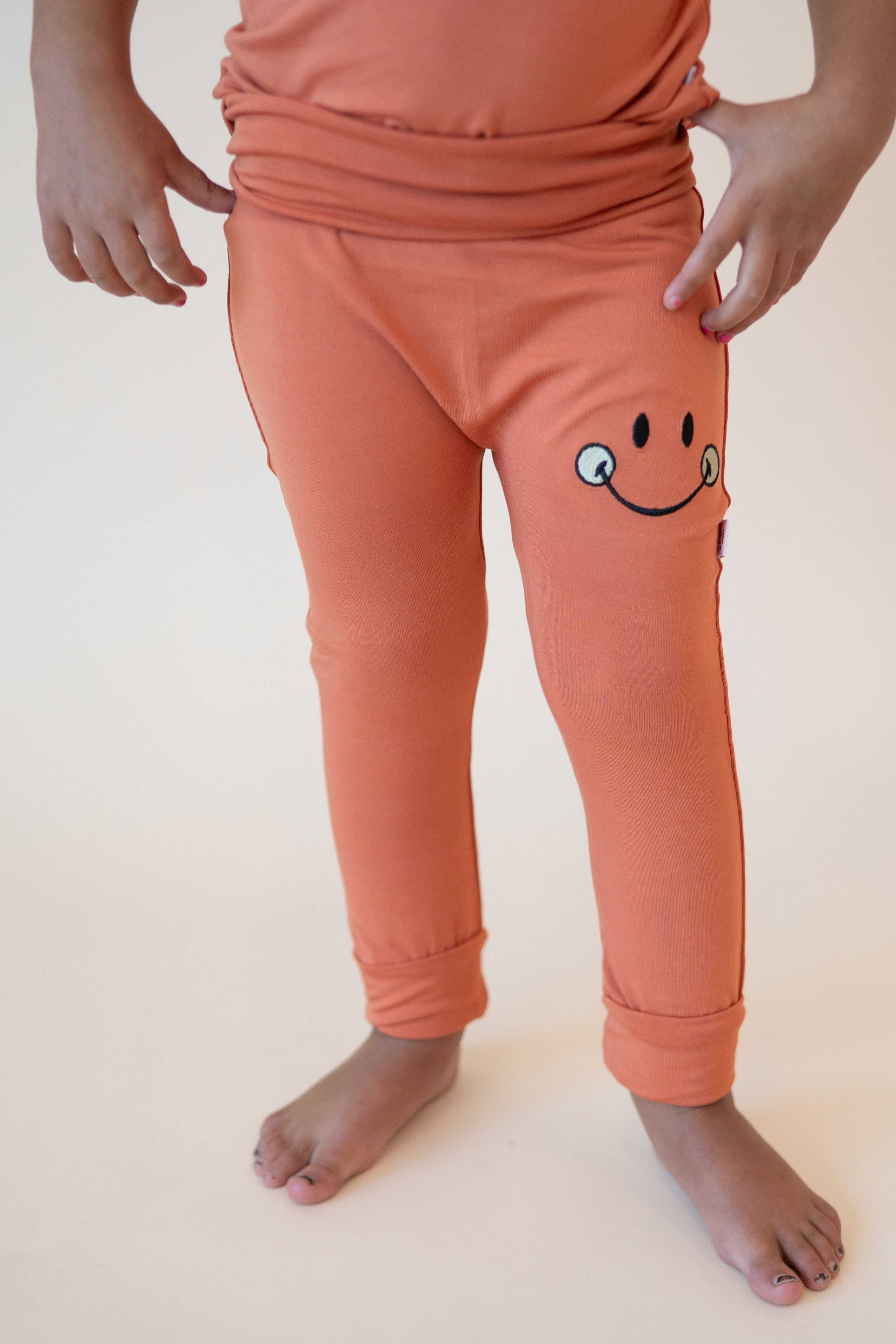 Orange bamboo pants with a smiley face graphic and adjustable cuffs.