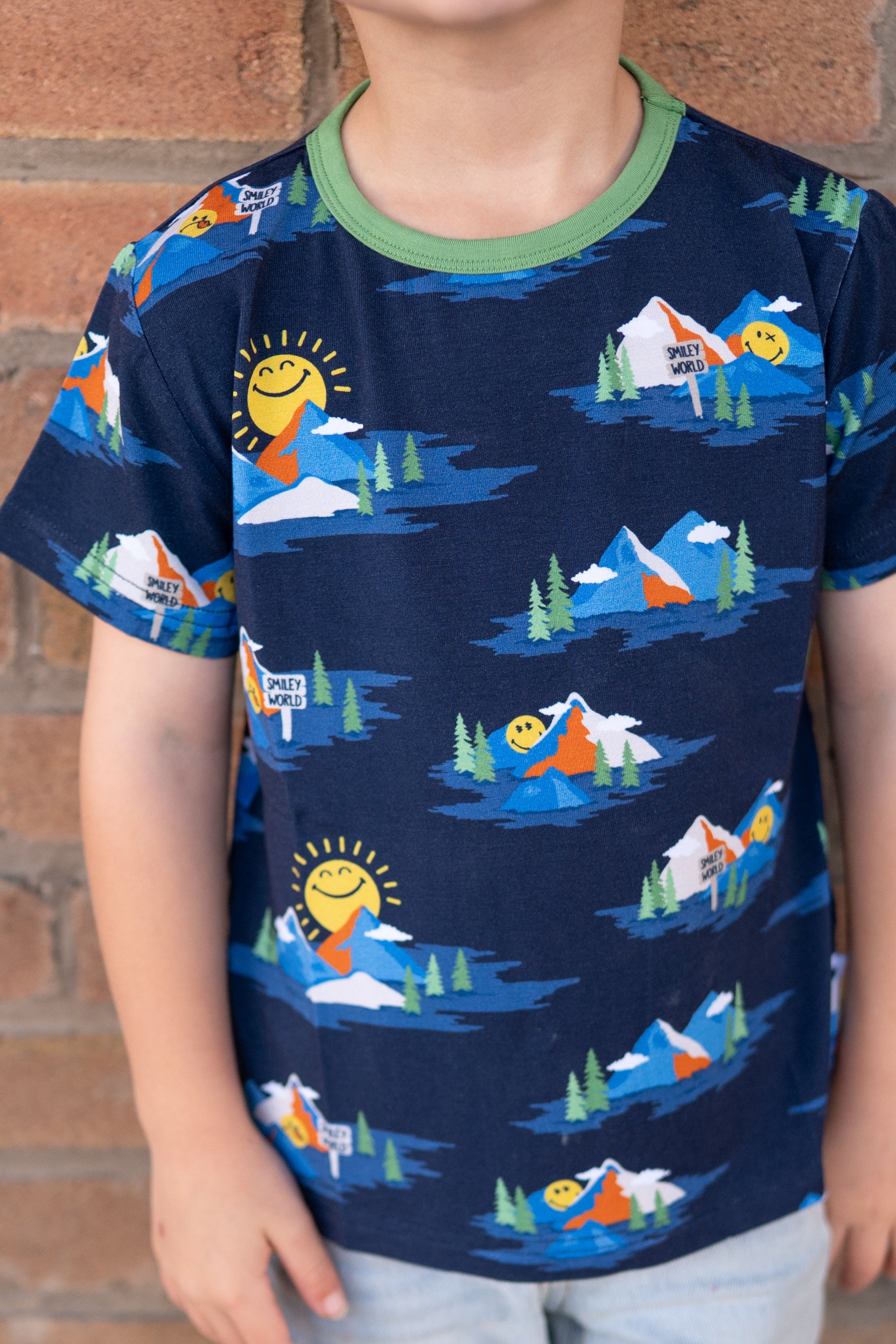 A child wears a navy t-shirt with a colorful mountain and smiley face print.