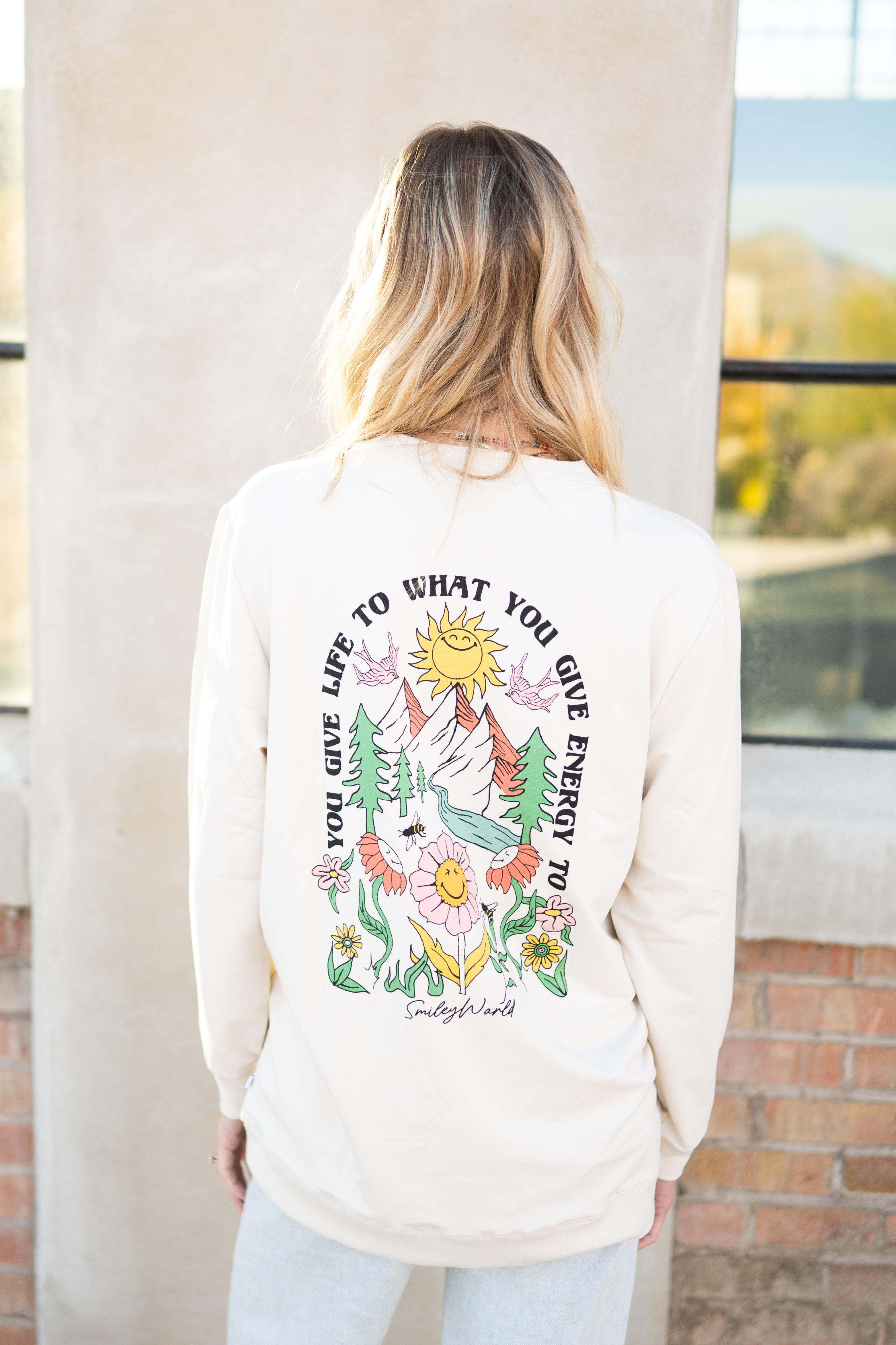 Cream crewneck sweatshirt with a colorful SmileyWorld graphic on the back.