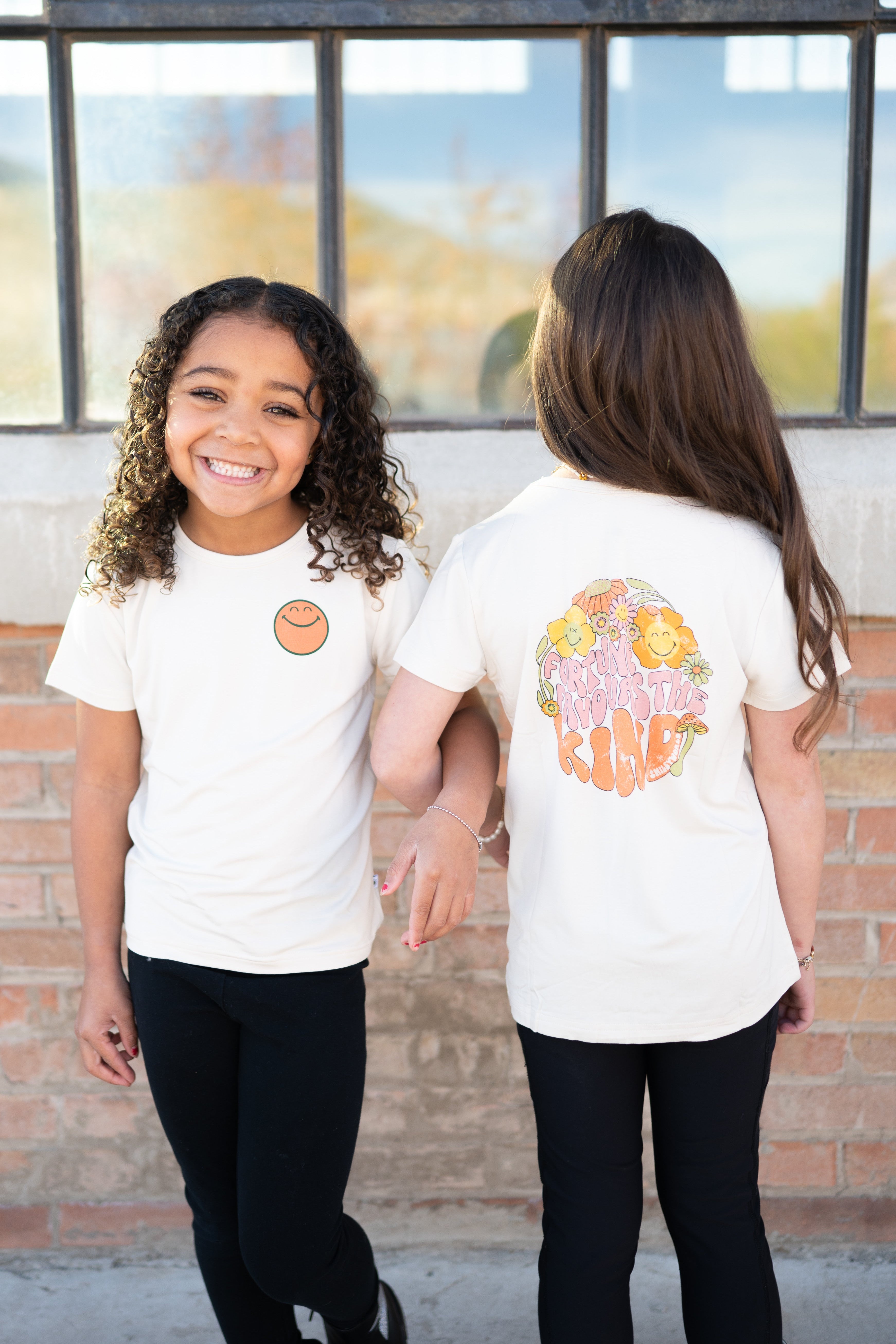 Two girls in white t-shirts with smiley face graphics stand together.
