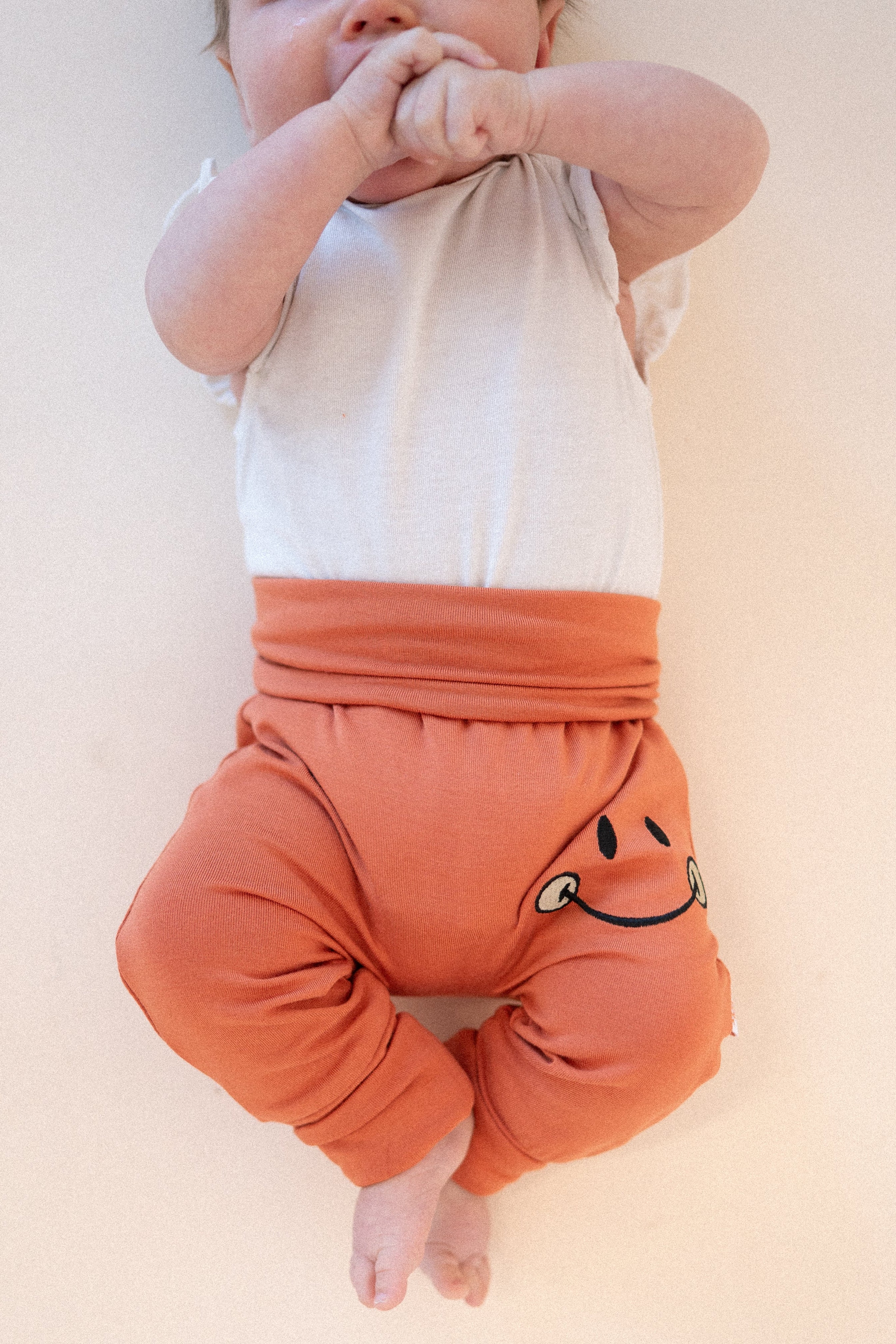 Baby pants in rust colored bamboo with a mini smiley face embroidered on the leg.