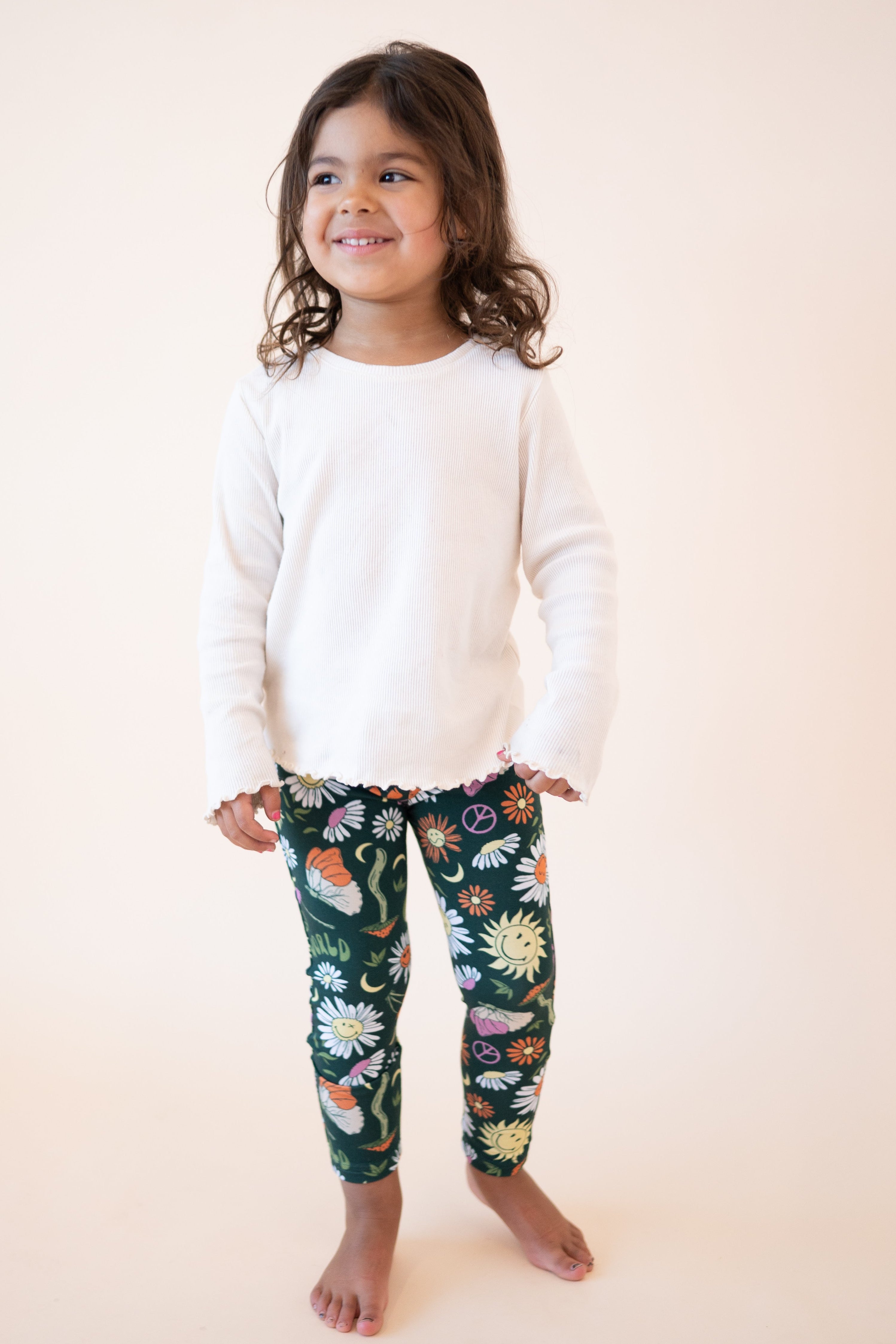 A young girl wears a white long-sleeved shirt and green leggings with a groovy floral SmileyWorld print.