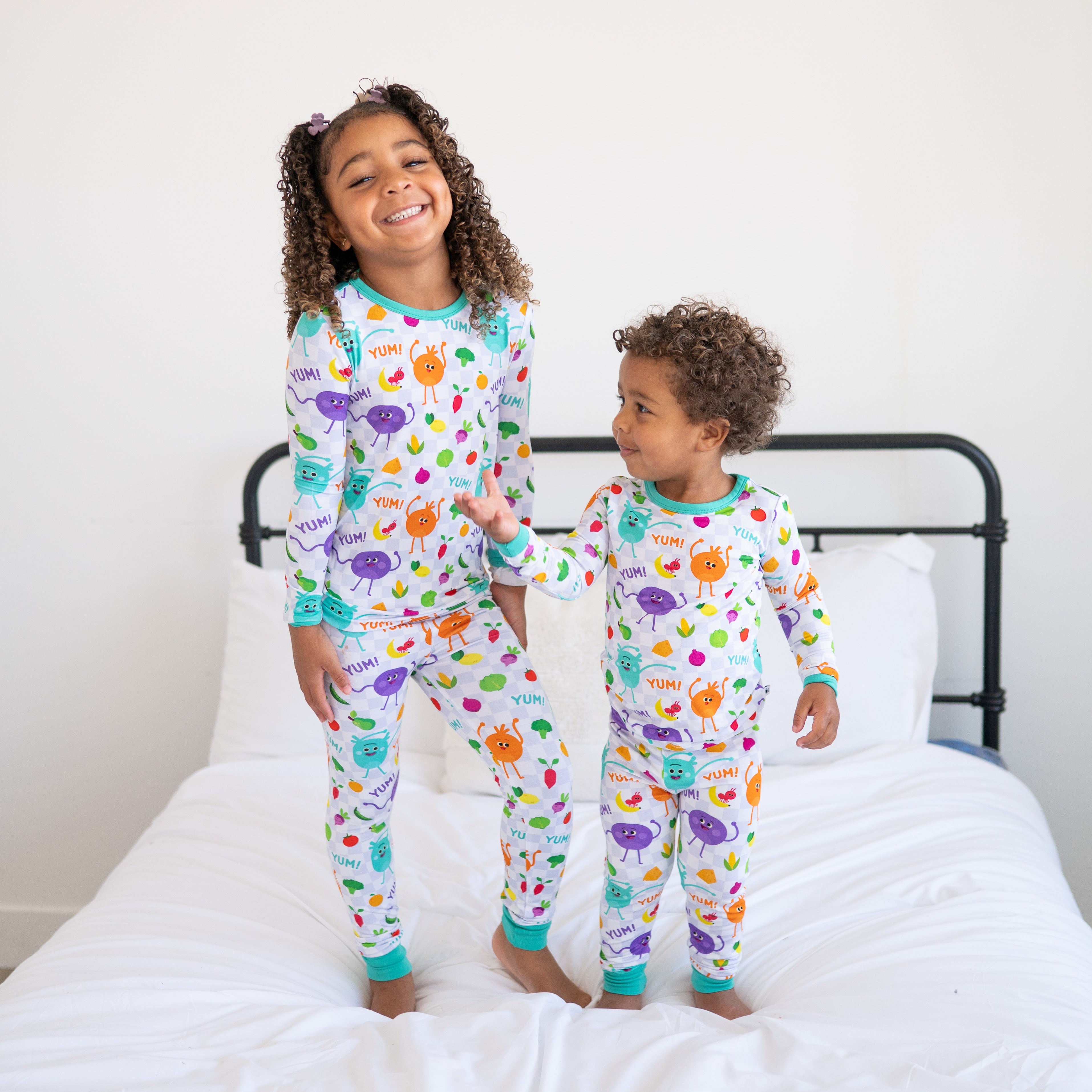 Two children in matching pajamas with a checkered pattern and cartoon vegetables.