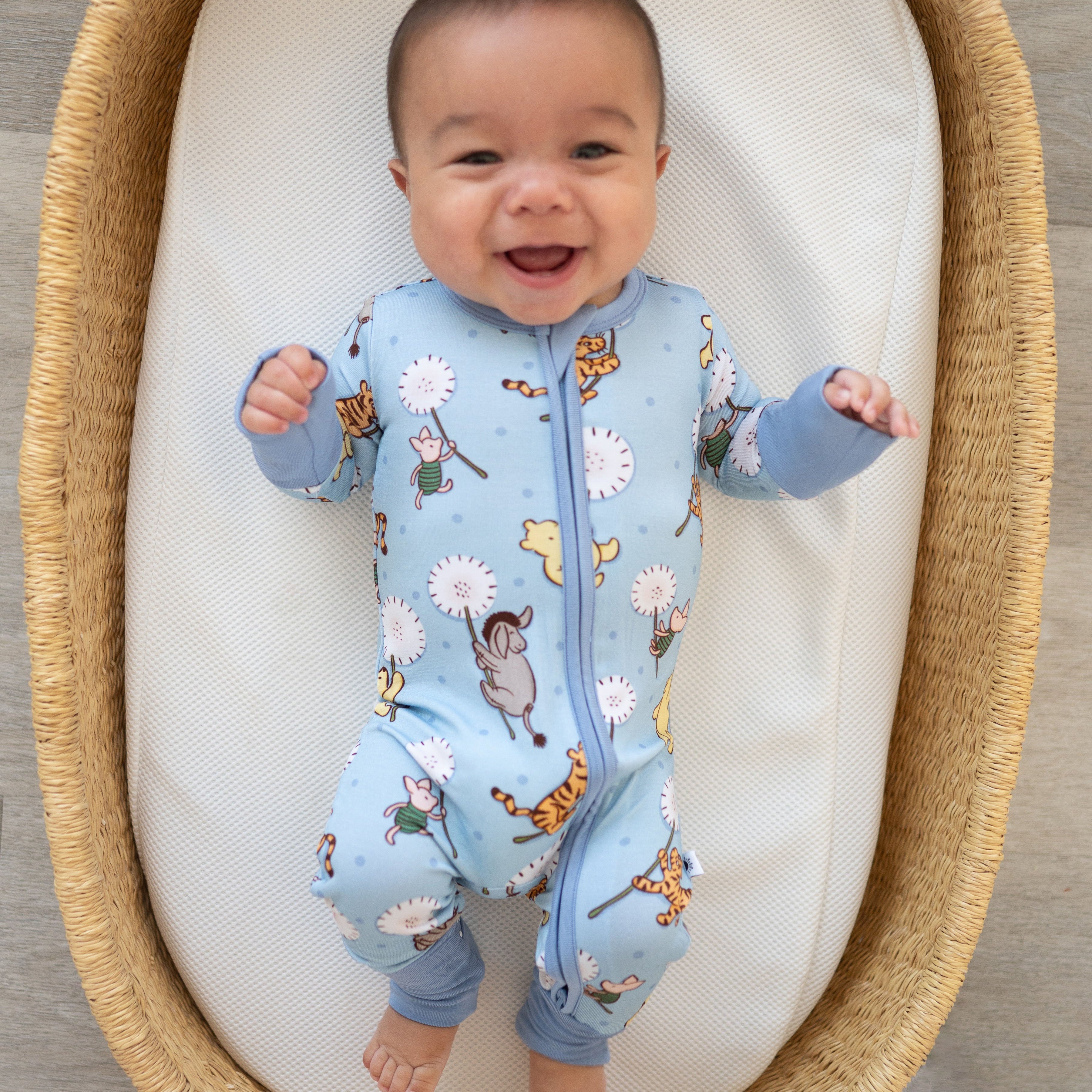 Baby in a blue onesie with animal prints in a wicker crib.