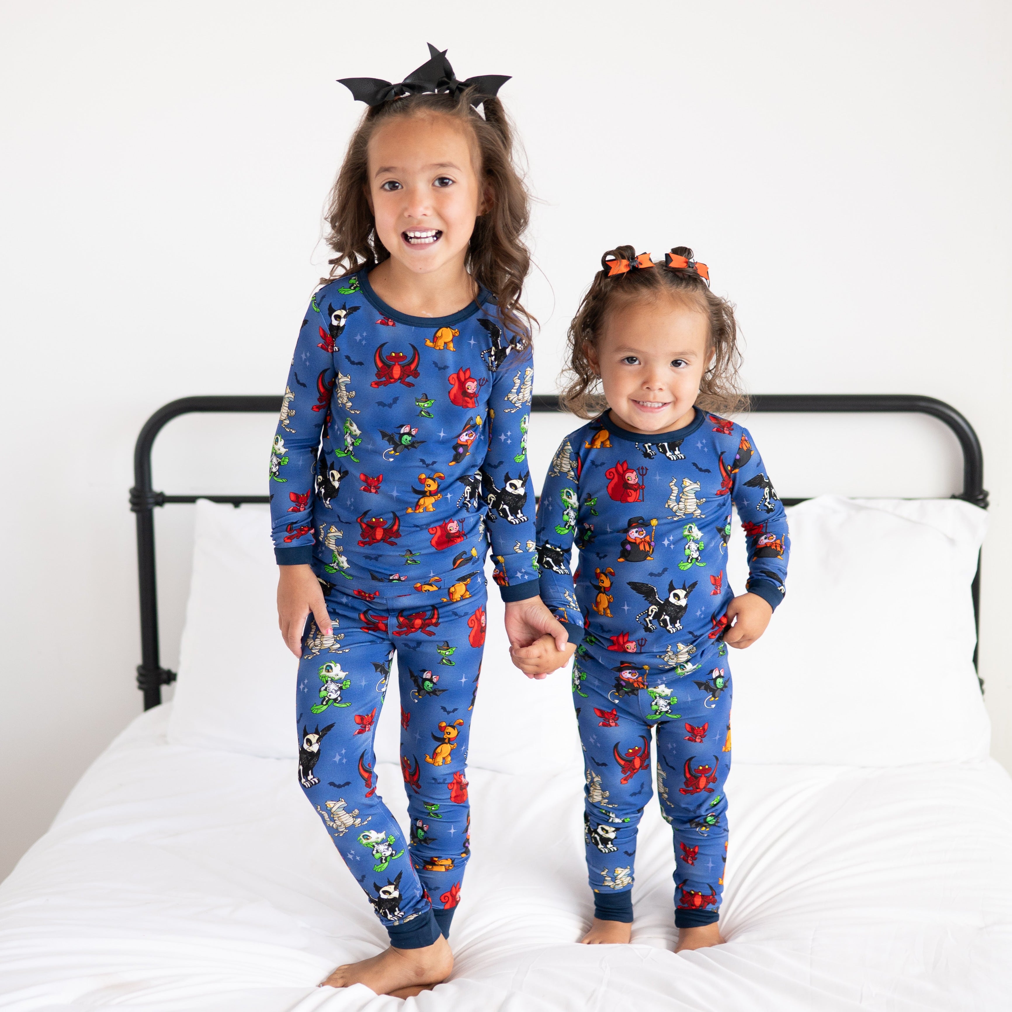 Two young girls in blue Halloween Neopets pajamas stand on a bed.