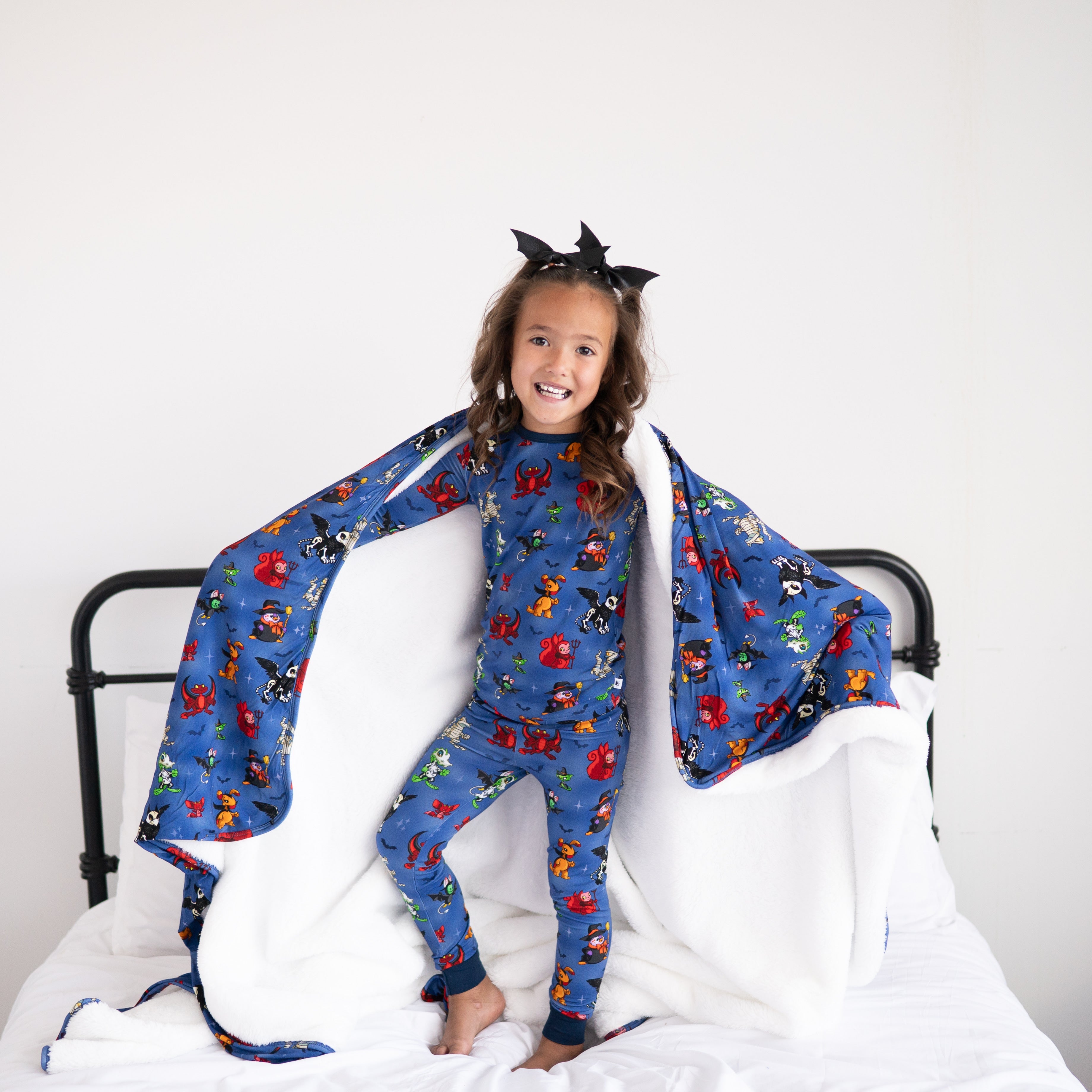 A young girl wears Halloween-themed pajamas with bat wings and a matching blanket.