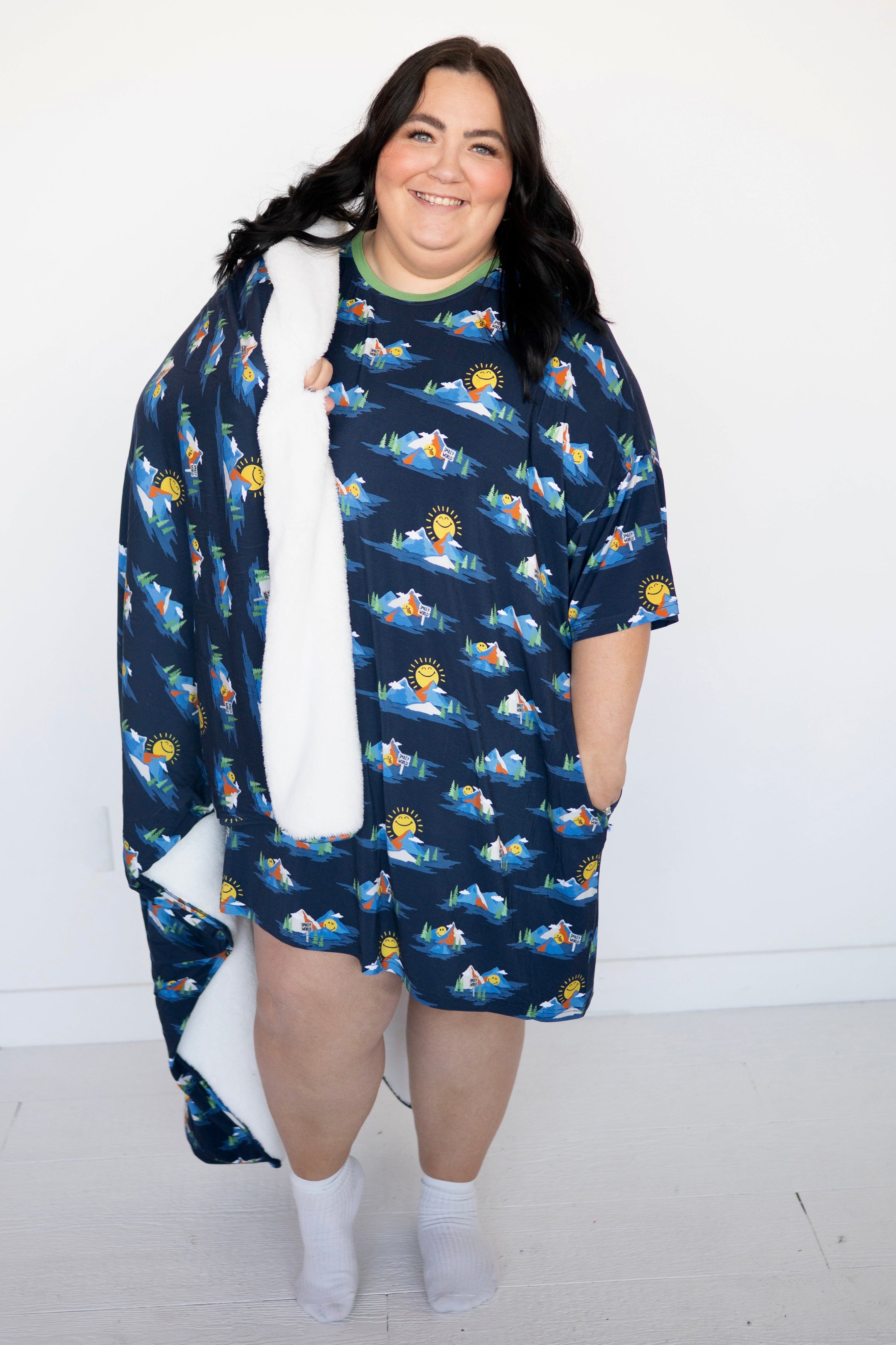 A woman wears a navy blue oversized sleep tee with a Mount SmileyWorld print and white fuzzy trim.