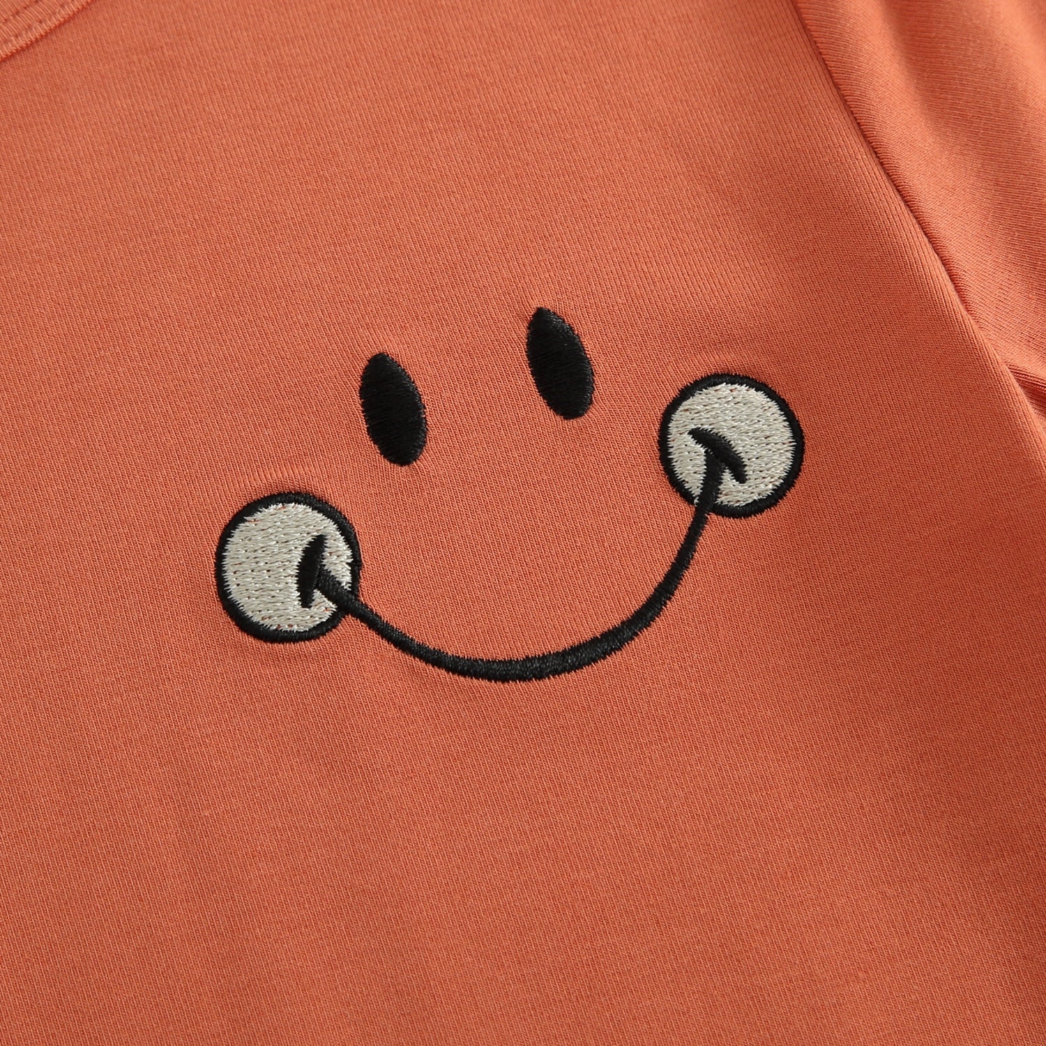 T-shirt with embroidered smiley face on rust colored bamboo fabric.