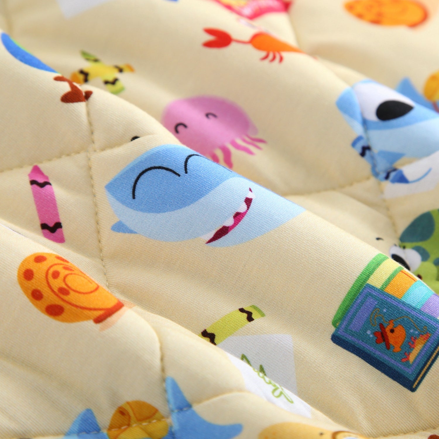 A light yellow quilted blanket with a pattern of cartoon sea creatures and school supplies.