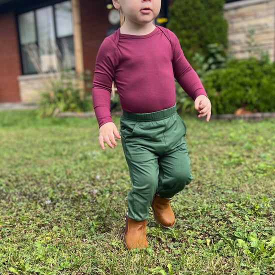 Child dressed in the Burgundy Bamboo Bodysuit paired with green pants
