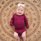 Baby girl resting on a rug in the Burgundy Long Sleeve Bamboo Bodysuit
