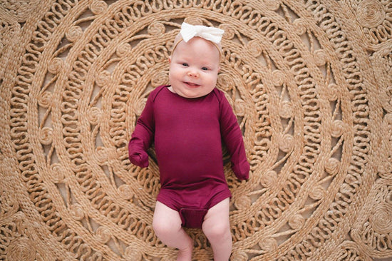 Baby girl resting on a rug in the Burgundy Long Sleeve Bamboo Bodysuit