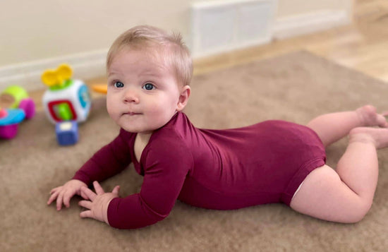 Infant lying down wearing the Burgundy Long Sleeve Bamboo Bodysuit